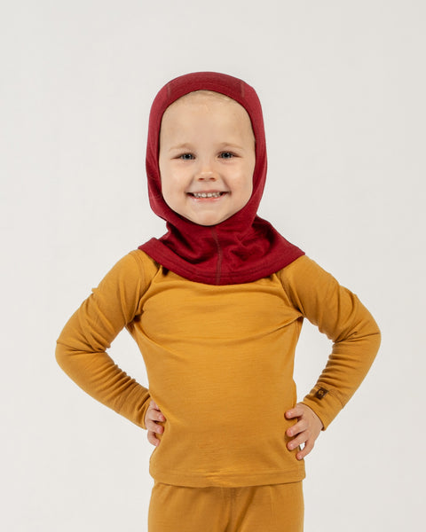 Child wearing a spicy yellow menique outfit with a royal cherry merino balaclava on a light gray background