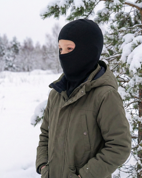 Child wearing black merino wool balaclava and winter jacket in snowy forest