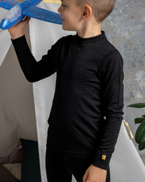 a boy playing with an airplane toy, wearing the menique Kids' 160 Thermal Long Sleeve Crew in Black color.