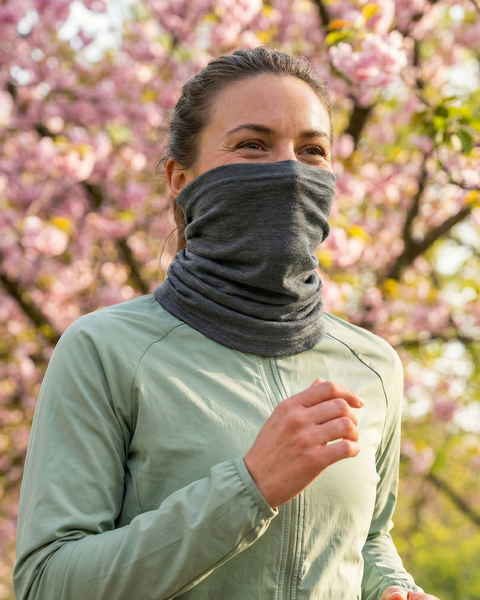 Woman wearing gray merino wool long neck gaiter while jogging outdoors in spring, breathable temperature-regulating face and neck protection for active lifestyle