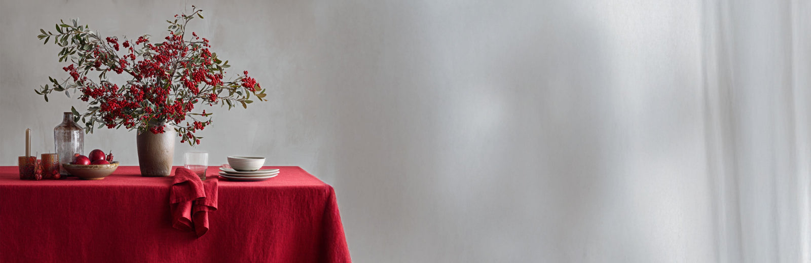 Table setting with a red tablecloth, flowers, and candles against a plain wall.