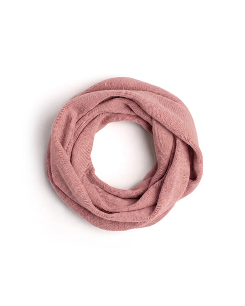 A pink knit infinity scarf coiled into a neat circle on a white surface.