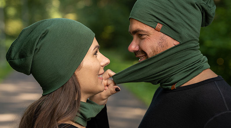 Couple outdoors wearing dark green merino wool gaiter and beanie.
