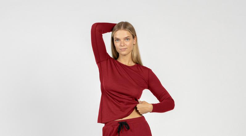 A woman wearing the menique merino wool long sleeve shirt in royal cherry, color, with one hand on her waist and the other above her head.