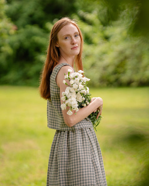 The model is standing sideways, holding a bouquet of wildflowers. This photograph accentuates the length of the green gingham crop top.