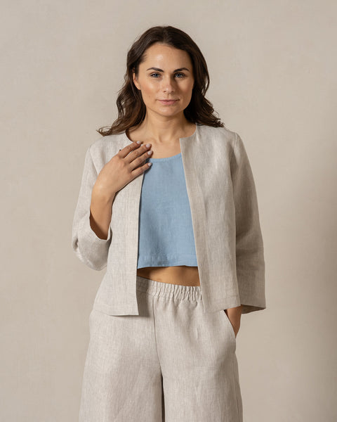 Woman wearing a natural linen jacket and pants with a blue top against a plain background