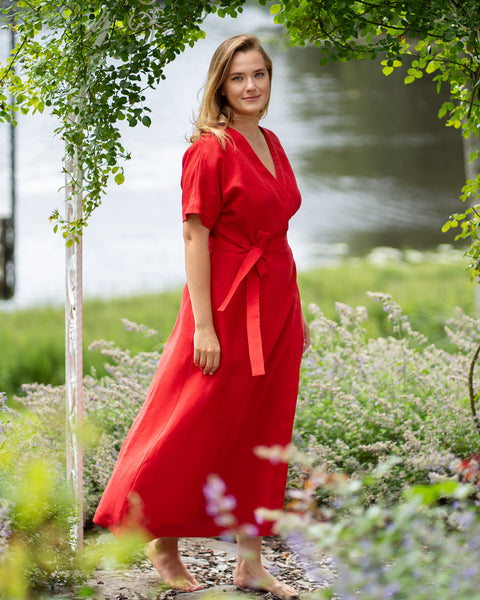 Woman in red wrap maxi dress standing in garden by lake, flowing feminine summer dress with waist tie