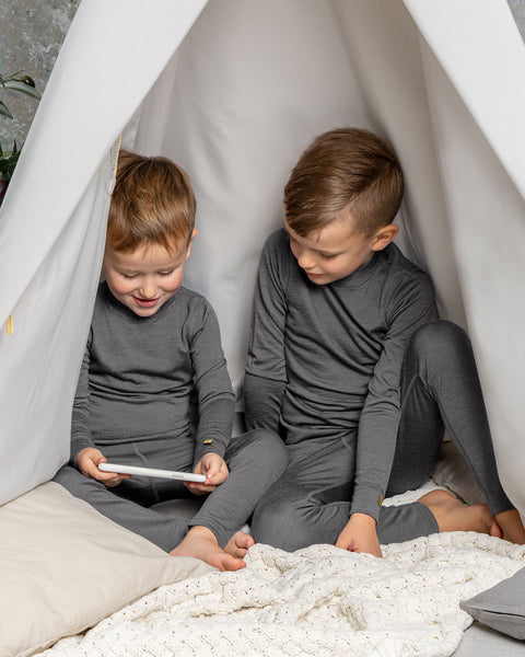 Two boys in gray Merino wool base layers sitting inside a play tent, looking at a tablet.