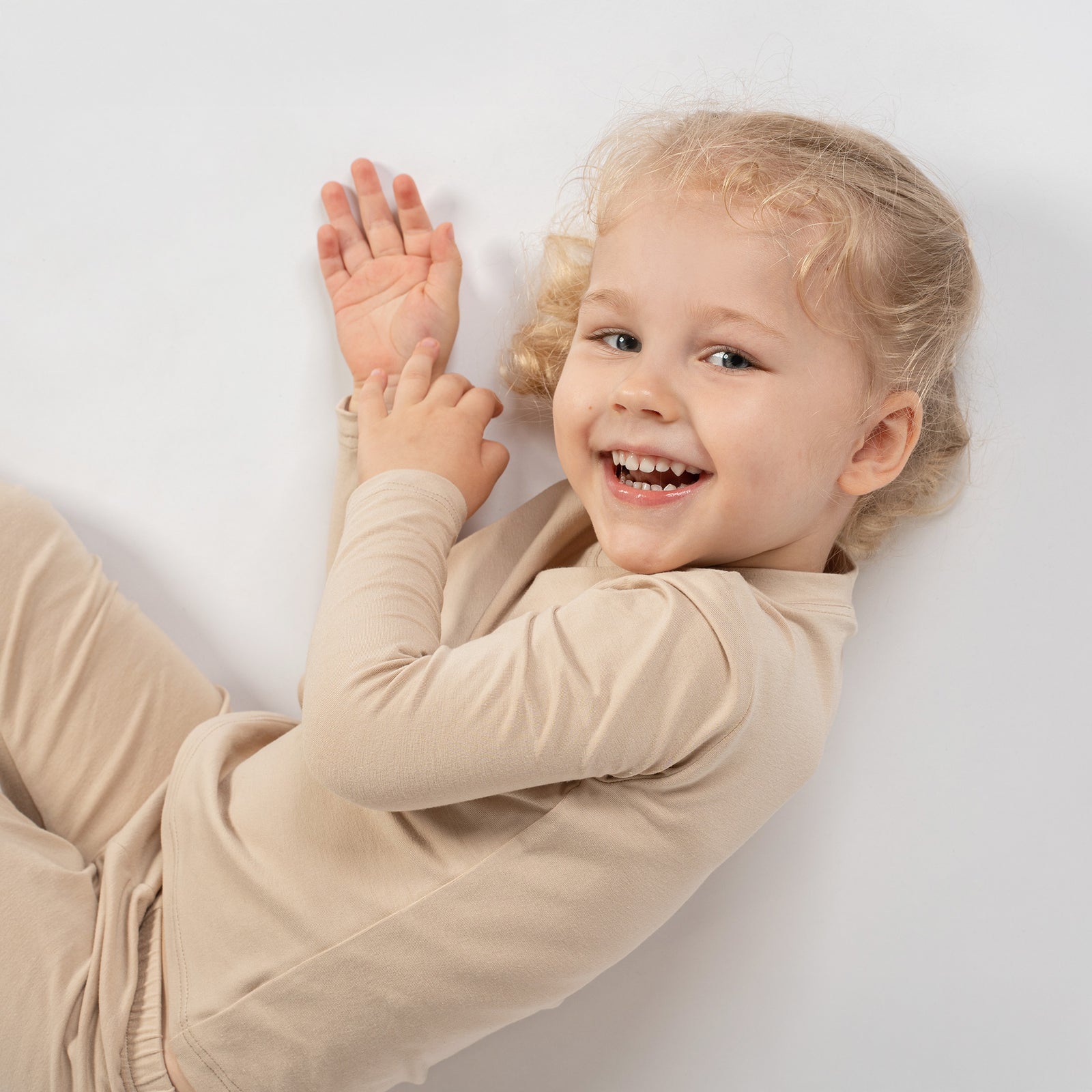 Girl sitting cross-legged in beige bamboo long-sleeve top and bottoms, next to a small brown poodle with a pink hair tie.