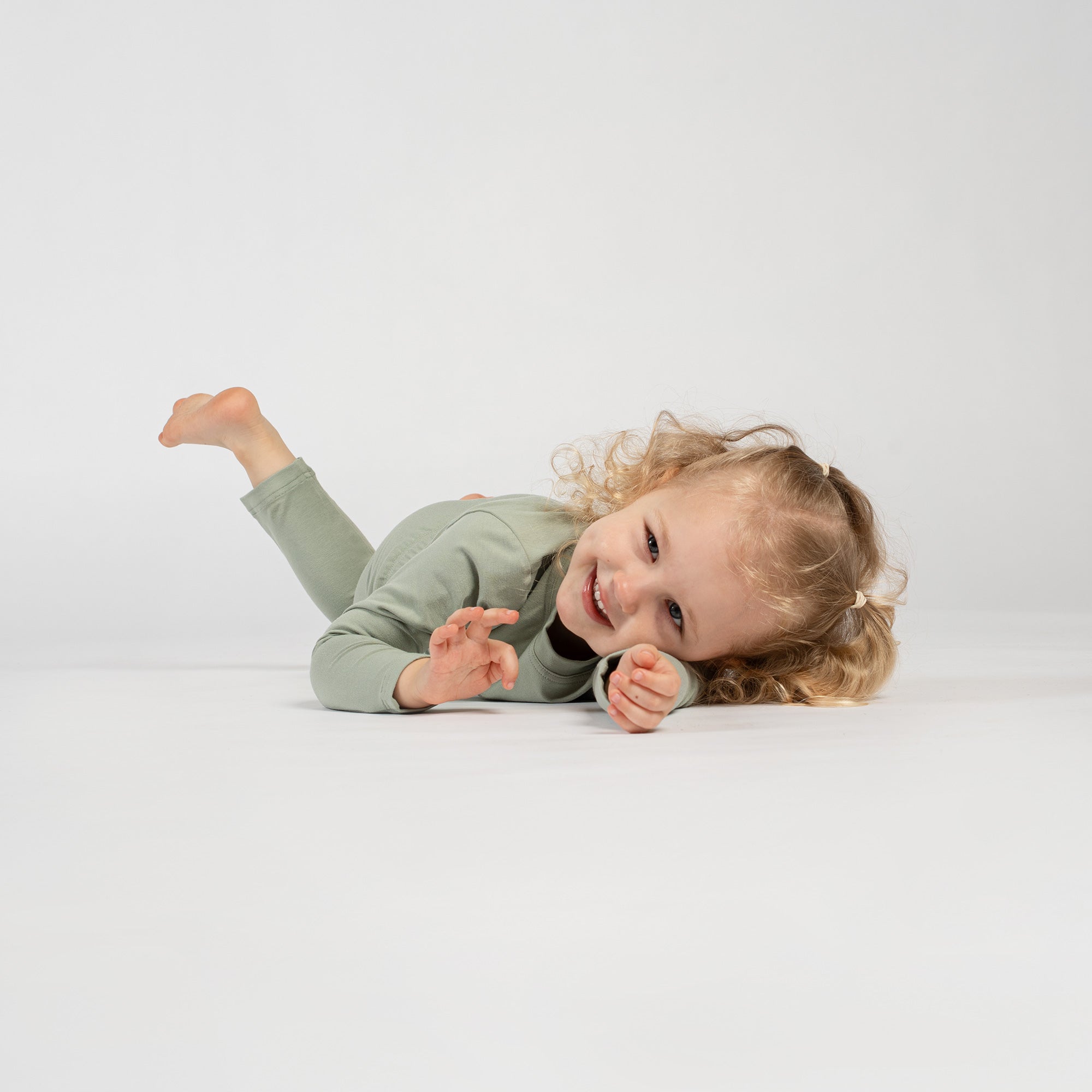 Happy child standing in green bamboo long-sleeve top and bottoms, barefoot.