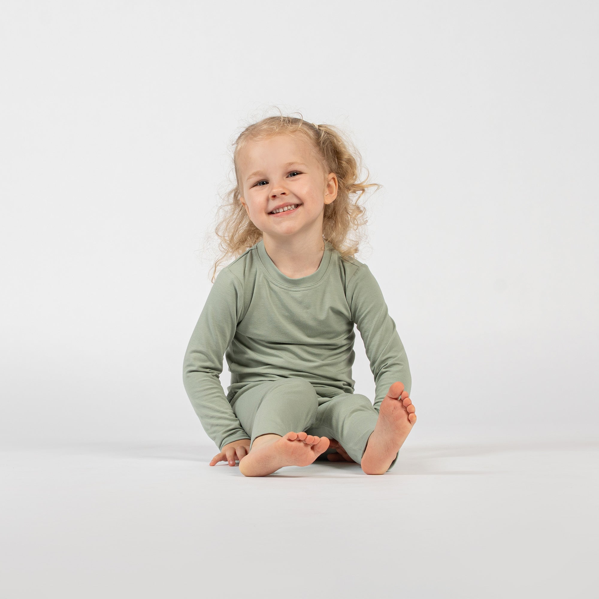 Laughing child lying on the floor in beige bamboo long-sleeve top and bottoms.