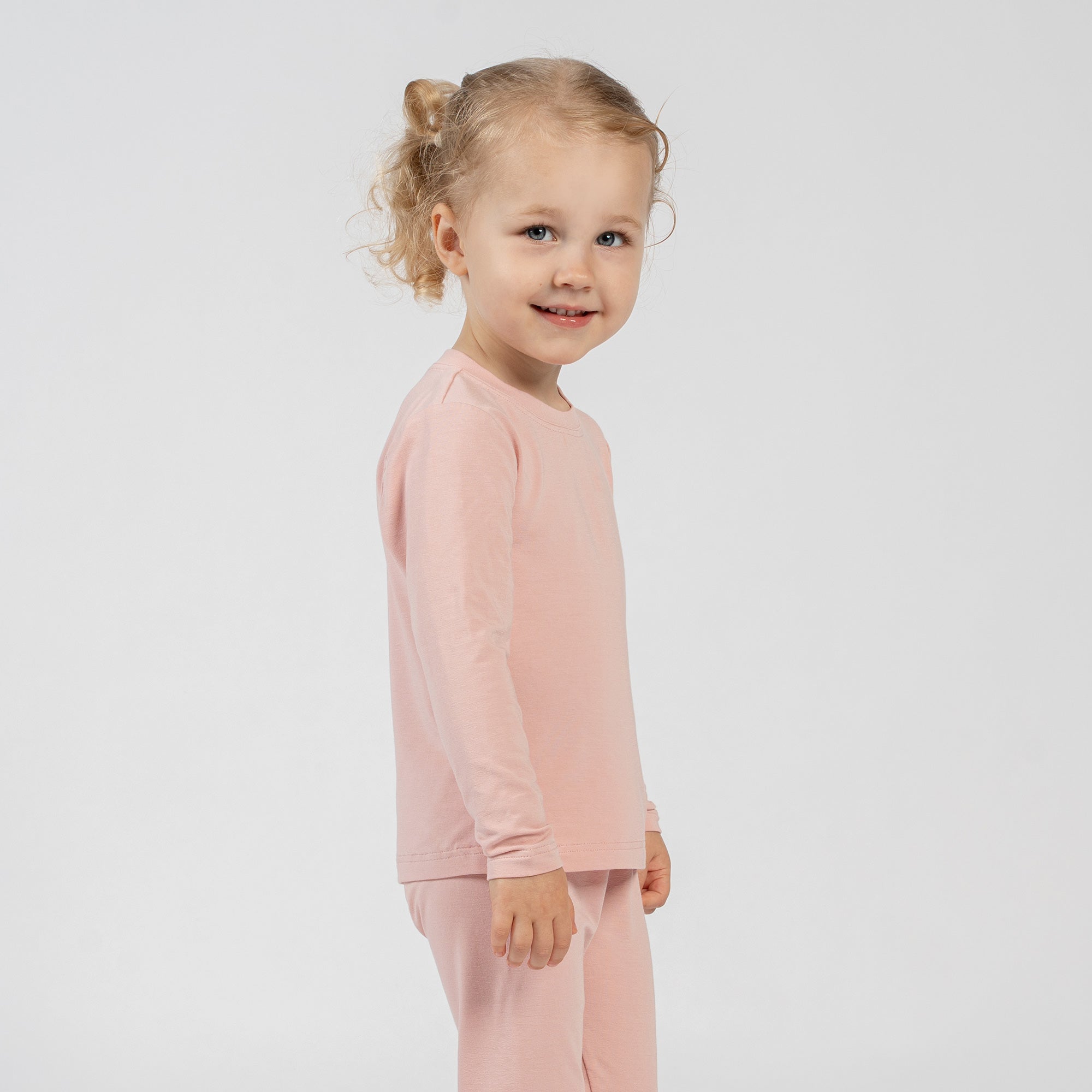 Smiling child sitting on the floor in pink bamboo long-sleeve top and bottoms.