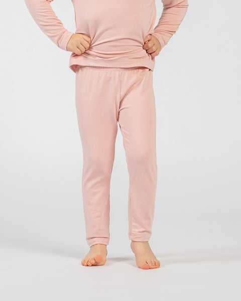 Child wearing pink bamboo long-sleeve top and matching pants, standing barefoot against a plain light background with hands resting on the waist.