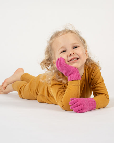 A young child with curly blonde hair and a bright smile wearing pink gloves on a white background