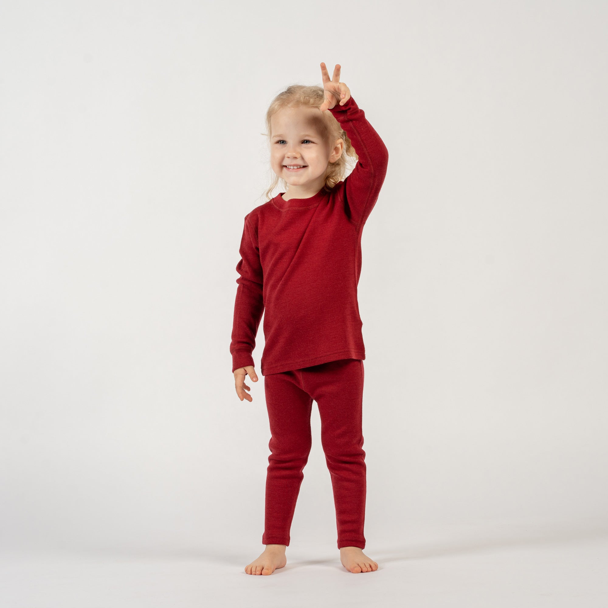 Two children, a boy and a girl, standing close to each other wearing a cherry royal merino long sleeve top and matching pants. The girl has her arms around the boy.
