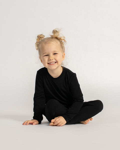 Child sitting on the floor wearing black bamboo base layer set with long sleeve top and leggings.