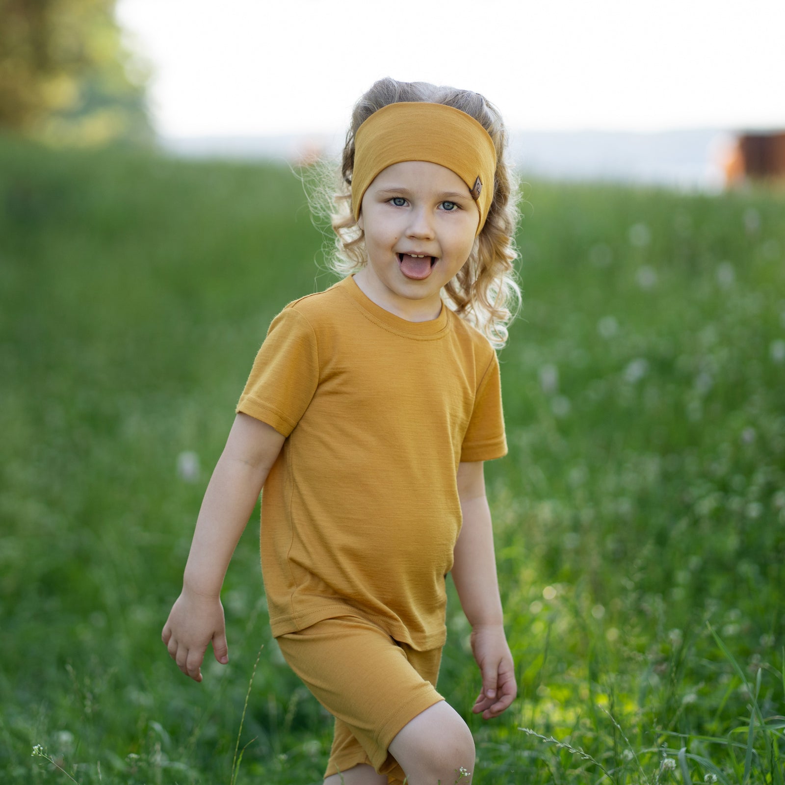 Two children standing hand in hand outdoors wearing matching Merino wool T-shirts and shorts in yellow and dark green. The lightweight, breathable kids' outfits are showcased in a sunny park setting, perfect for everyday play, family outings, and warm-weather adventures.
