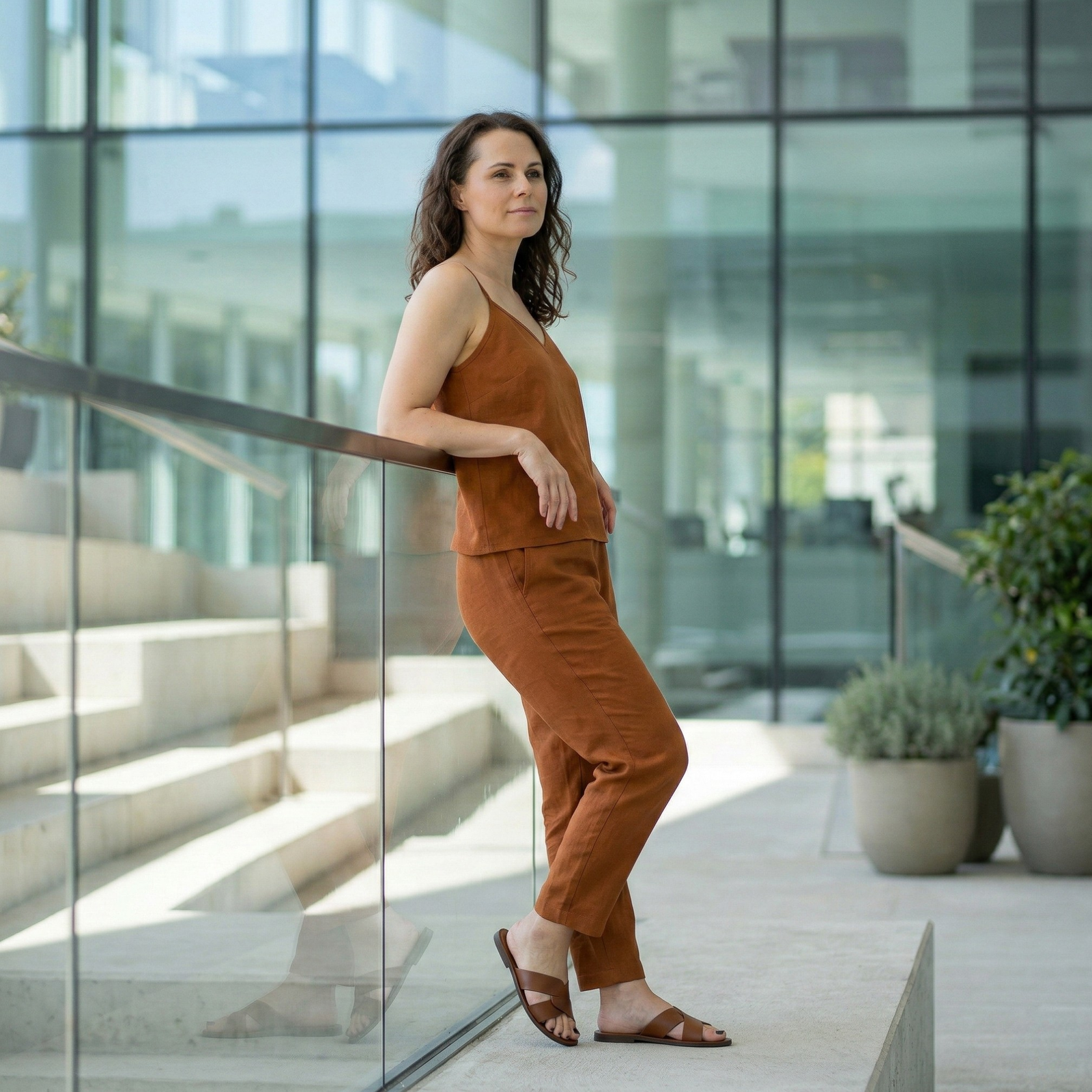 Woman wearing almond brown linen camisole top and matching linen pants, breathable lightweight summer co-ord set styled outdoors in modern setting