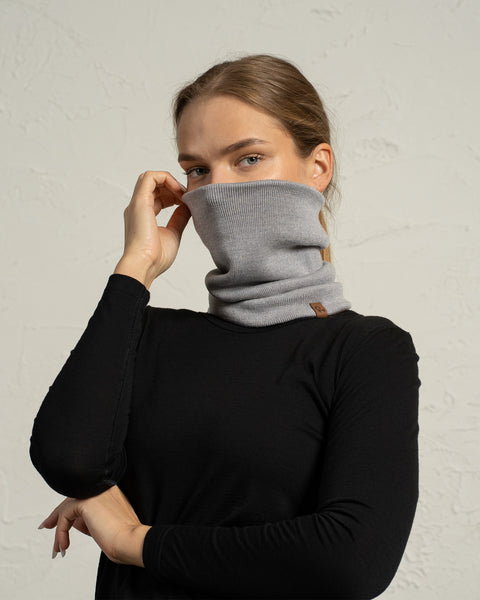 Woman wearing light gray knit Merino neck gaiter pulled over nose, breathable winter face and neck warmer.