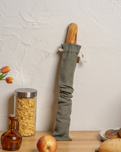 Long Bread bag hanging on a hook with bread and kitchen items on a table.