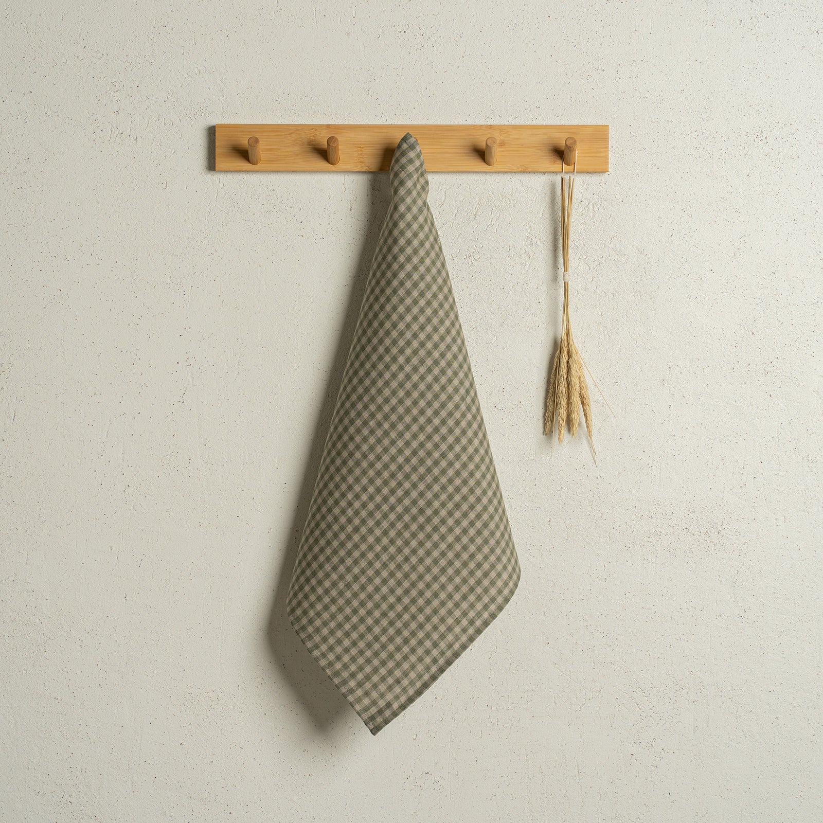 The menique square linen dish towel in color dark green hanging on a wooden rack on a wall.