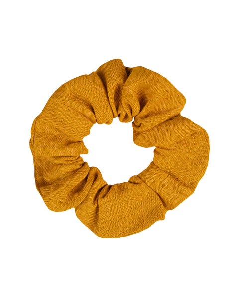 A top-down view of a mustard yellow fabric hair scrunchie isolated against a pure white background. The fabric has a slightly textured, linen-like appearance and is gathered around an internal elastic.