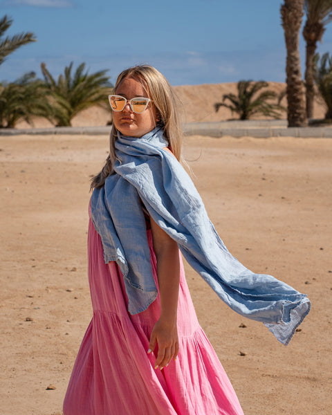 Women wearing Linen Scarf in Cloudy Blue color while in the background is seen palm trees