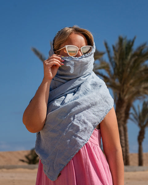Women wearing Linen Scarf in Cloudy Blue color while in the background is seen palm trees