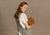 A woman wearing a green and white checkered linen Japanese-style apron from menique over a white short-sleeved blouse holds a bunch of dried berries, standing against a neutral beige background.