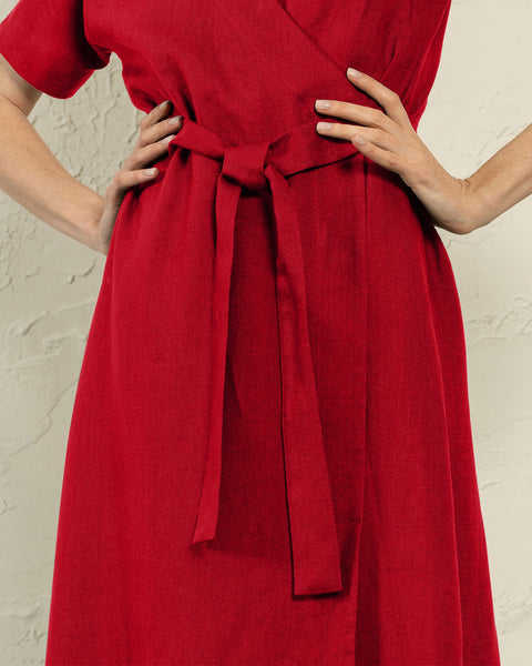 A close-up shot of a person wearing a red dress with a tied belt at the waist. The person&#39;s hands are resting on their hips, and the dress is the main focus of the image.