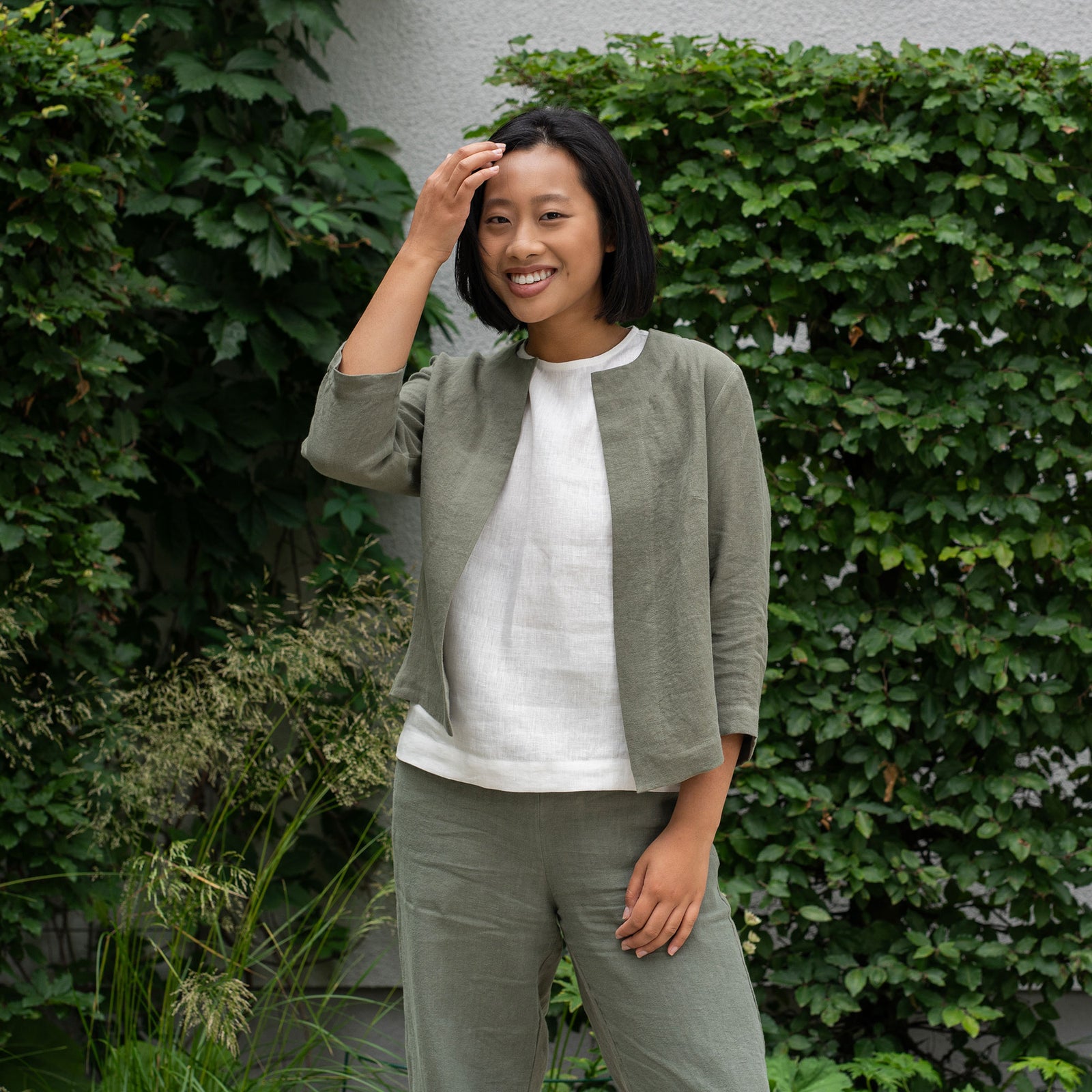 Woman wearing a natural linen jacket and pants with a blue top against a plain background