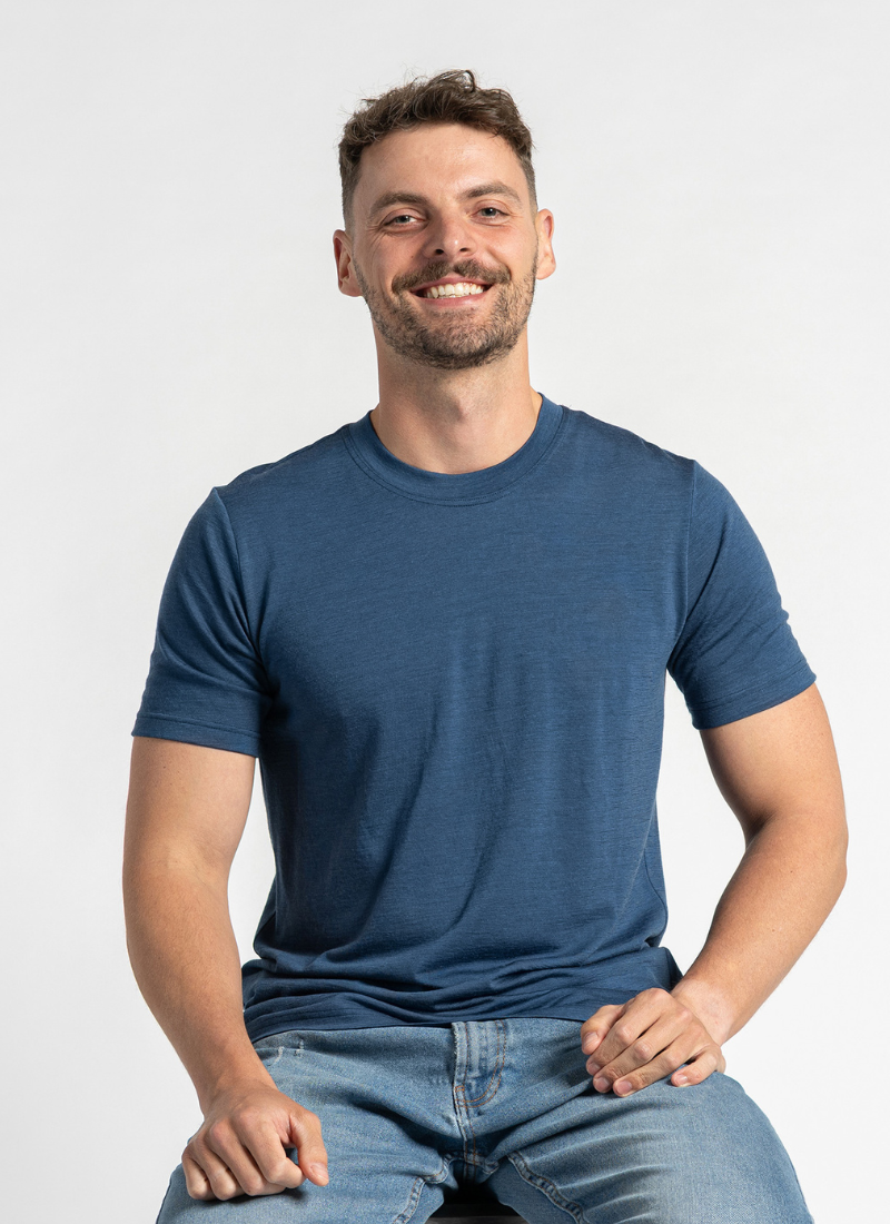 Man wearing a blue t-shirt and jeans sitting against a plain background