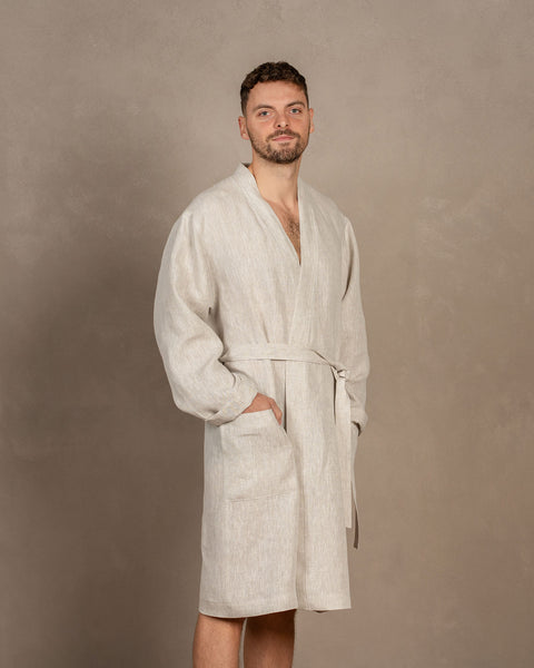 A man, turned slightly to the side, wearing the men&#39;s linen bathrobe in natural color. Both of his hands are in the side pockets.