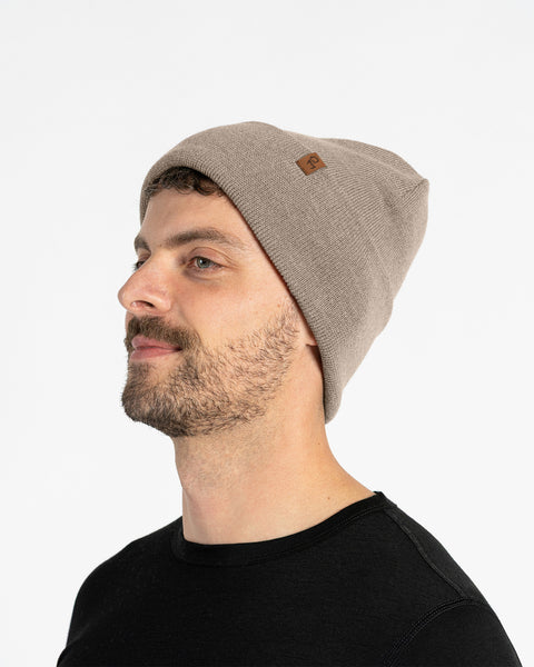 Man in side profile wearing a beige merino wool knit beanie with leather logo patch, clean white studio background.
