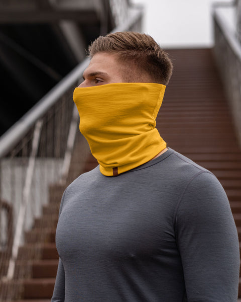 A man with short, blond hair is shown in a profile view, his gaze directed towards the left, as if lost in thought. He&#39;s wearing a vibrant spicy yellow neck gaiter that contrasts against his gray long-sleeved shirt. 