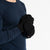 A person wearing a dark blue long-sleeved shirt and black menique mittens with a flap that can cover the fingers, turning them into mittens. The person is holding their hands together, and the flap on one glove is pulled back, exposing the fingers, while the flap on the other glove covers the fingers.
