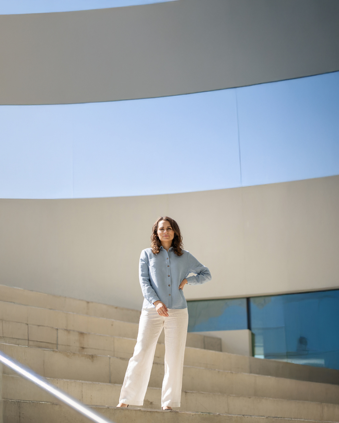 Woman standing on a modern architectural staircase with a clear blue sky.