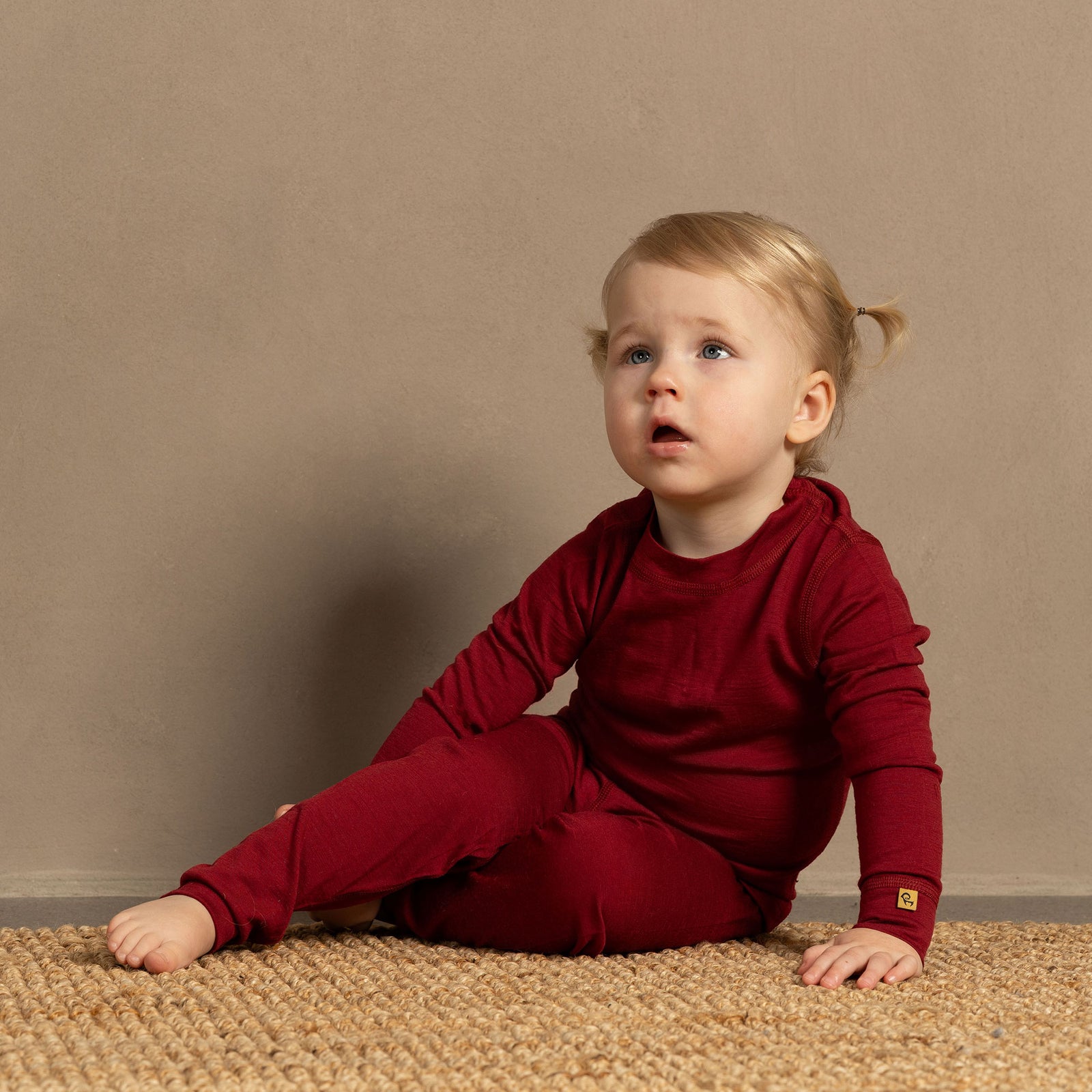 Happy toddler sitting in the crib, holding a book and wearing merino wool set.