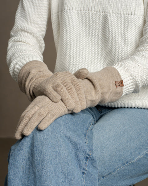 Person wearing creamy beige merino wool long gloves, hands resting on denim-clad knee, showcasing soft texture and comfortable fit.