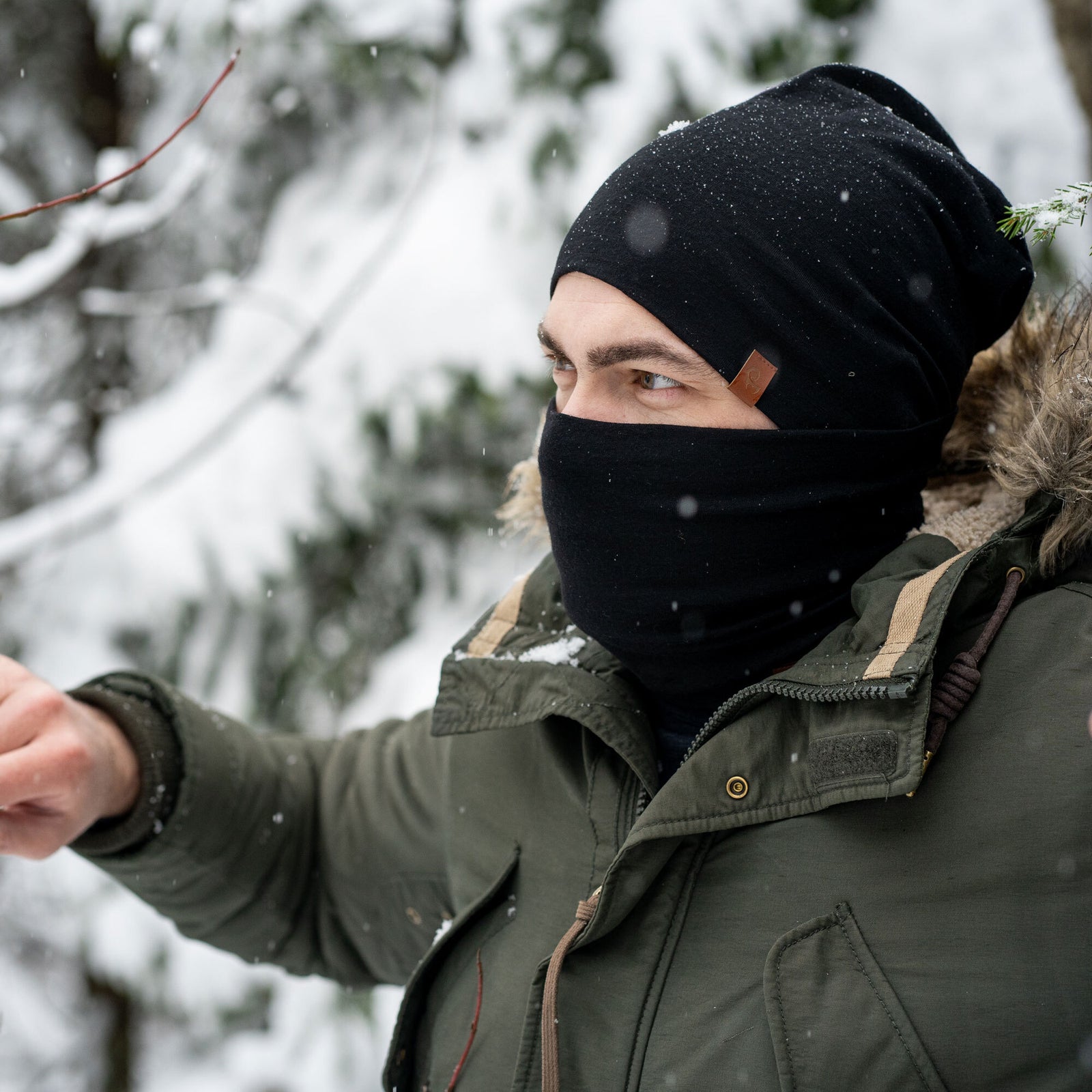 The Menique Men's Merino Beanie and Gaiter Set in Black color. The man is wearing the accessory set in a forest, in fall time.
