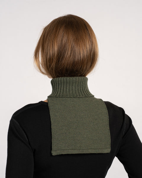 Back view of a woman wearing a dark green knitted merino wool dickie neck warmer over a black top.