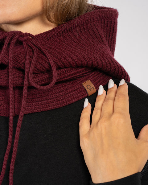 Close-up of royal cherry knitted merino wool hood balaclava with drawstrings and menique logo tag.