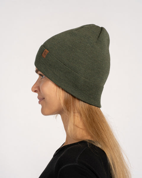 Side profile of woman in a dark green knitted Merino wool beanie, with long hair visible.