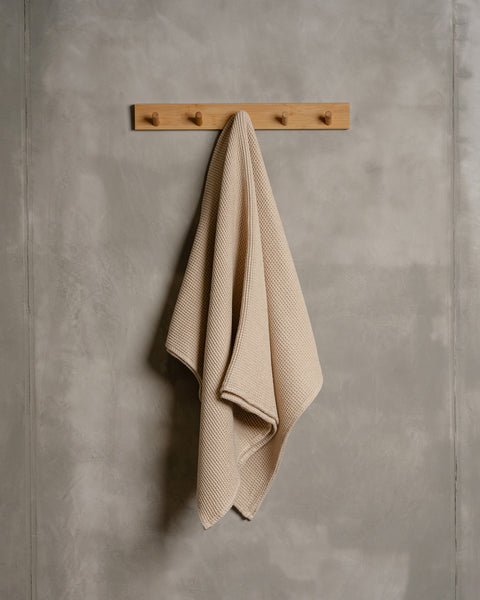 A linen &amp; cotton waffle body towel in sand brown color hanging on a wooden rack.