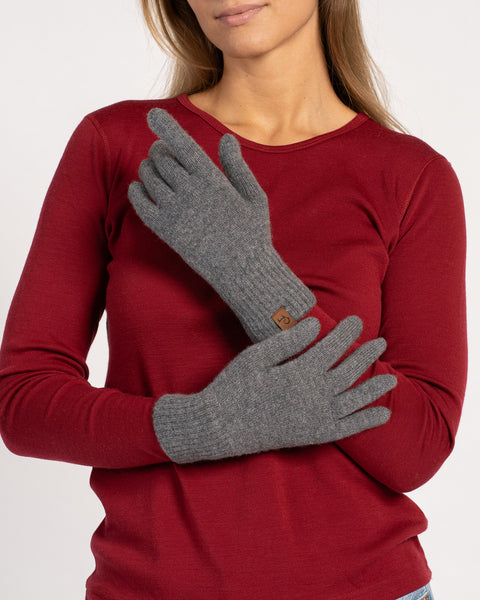 A woman in a red top wearing dark gray knitted cashmere short gloves, holding her arms crossed to show the glove’s fit and style.