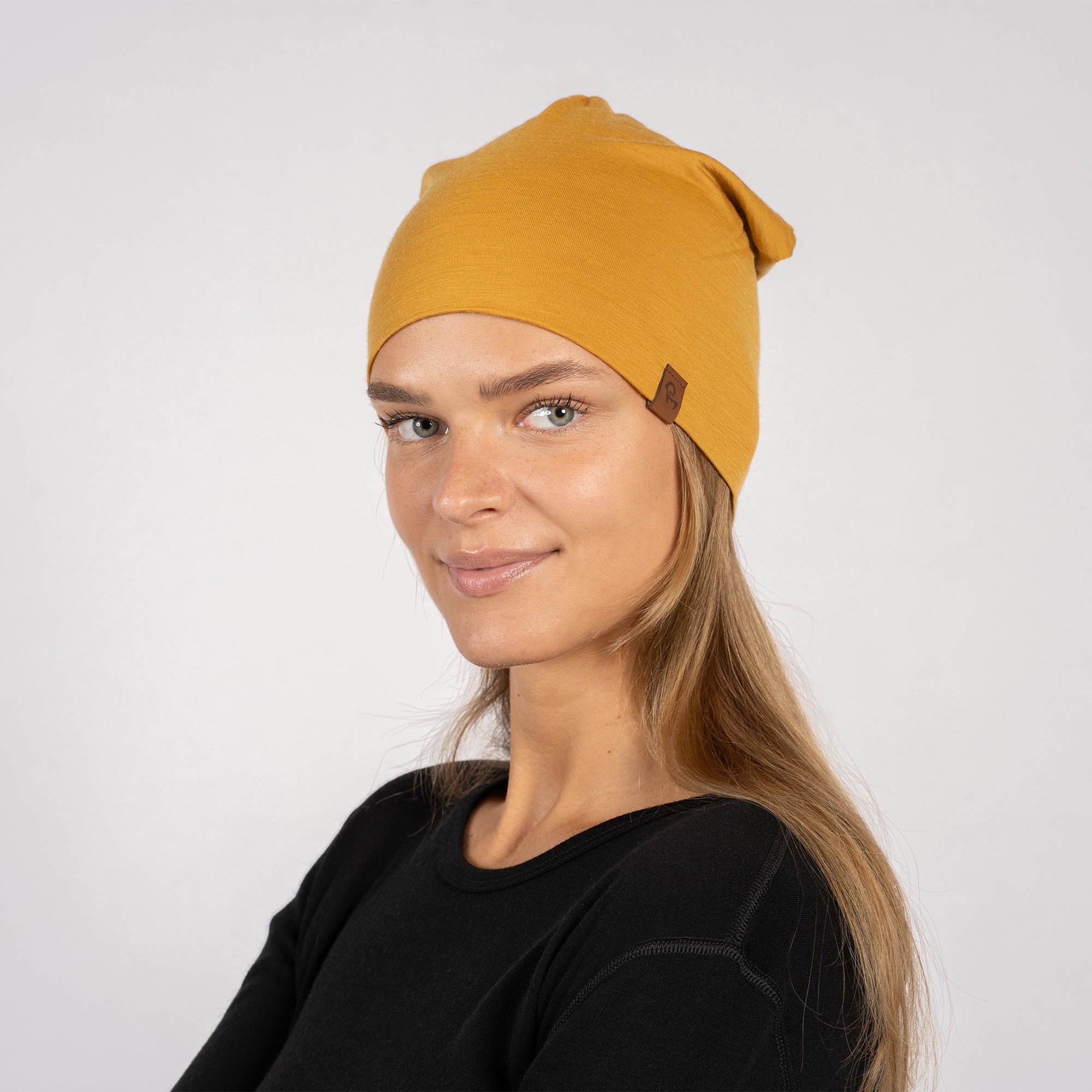 Close-up side view of woman in yellow merino beanie, touching her face gently.