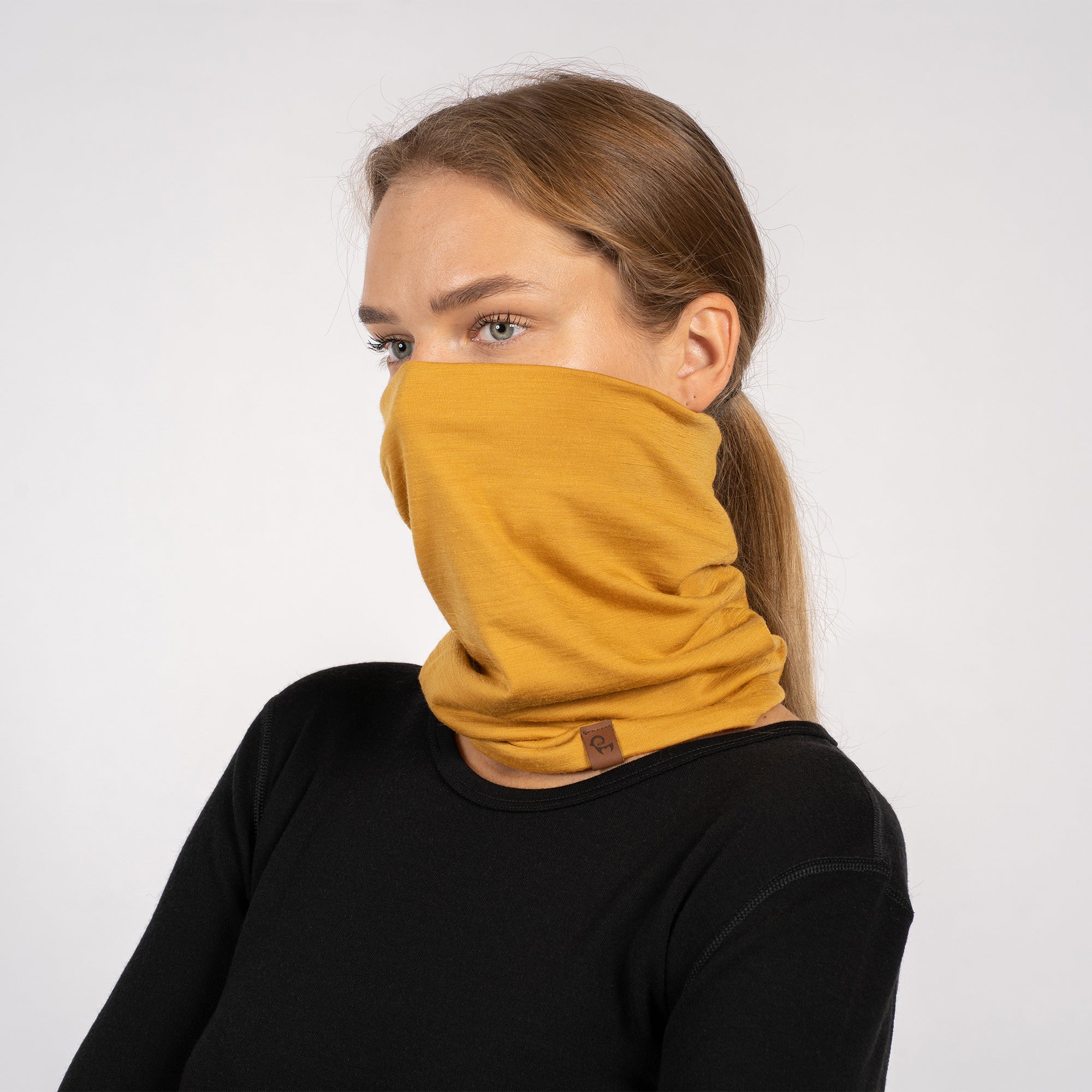 Yellow Merino wool neck gaiter pulled up over mouth and nose, woman in black top.