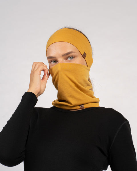 Woman adjusting yellow Merino wool gaiter while wearing matching headband.