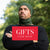 A person wearing a green beanie, neck gaiter, and black shirt poses with the text "GIFTS FOR MEN" overlaid in a red square.
