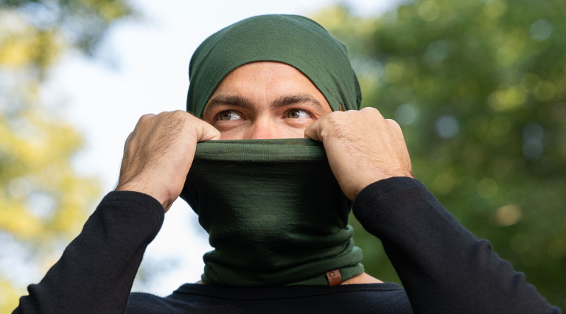 Man outdoors wearing dark green merino wool gaiter and beanie.